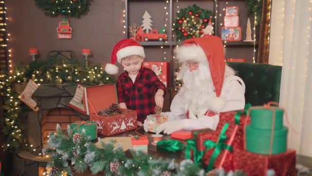 Weihnachtsmann und kleiner Helfer verpacken Tannenzapfen für Weihnachtsgeschenke. WEIHNACHTSKONZEPT NEUES JAHR — Stockvideo