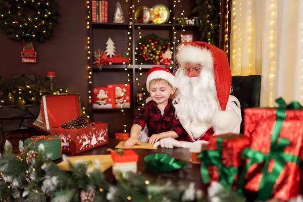 Маленький хлопчик відвідує Санту Клауса і допомагає йому відкривати конверти з різдвяними побажаннями. Святкова концепція — стокове фото