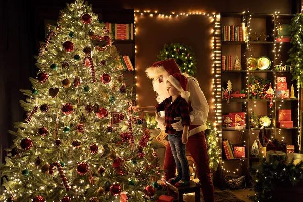 Santa Claus with little boy having fun by the fireplace while decorates Christmas tree — Stock Photo, Image