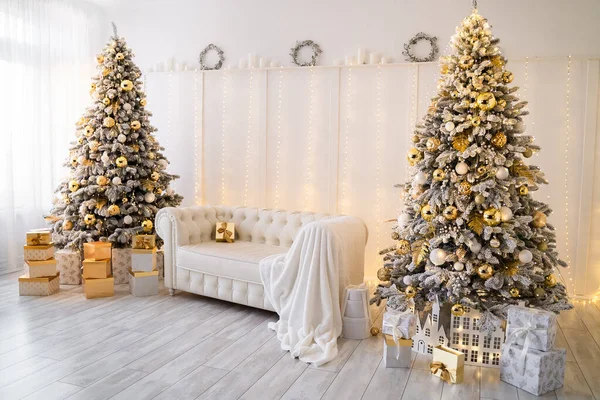 Interior de la sala de estar blanca con árboles de Año Nuevo decorados, cajas de regalo y sofá blanco. Color dorado —  Fotos de Stock