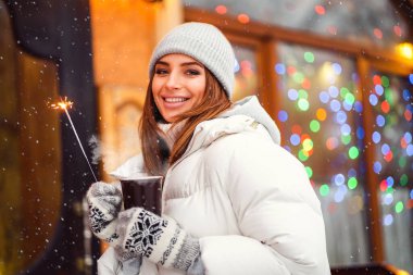 Neşeli güzel kız elinde kahve ve maytap tutarken Noel şehrinde yürüyor. Şenlik havası