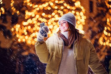 Neşeli yetişkin kız Noel süslerinin önünde dururken dışarıda selfie çekiyor.