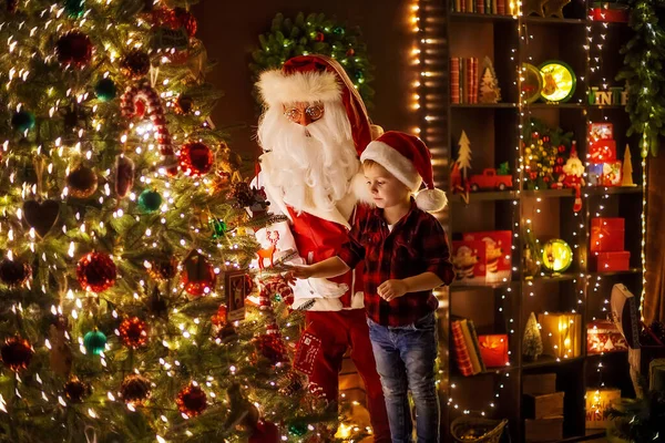 Санта Клаус прикрашає ялинку маленьким хлопчиком-асистентом. Новий рік, щасливе дитинство — стокове фото