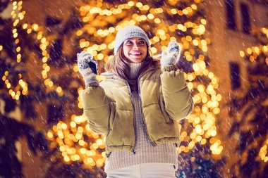 Heyecanlı mutlu kız dışarıda Noel süslerinin önünde telefonu duygusal olarak kullanıyor.