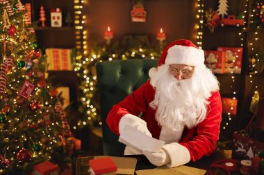 Noel Baba, masasında dilek listelerini okurken çocuklar için Noel hediyesi hazırlıyor.