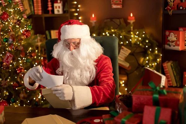 Weihnachtsmann bereitet am Schreibtisch Geschenke für Kinder für Weihnachten vor, während er Briefe mit Wünschen liest — Stockfoto