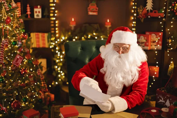 Der Weihnachtsmann bereitet am Schreibtisch Geschenke für Kinder für Weihnachten vor, während er Wunschlisten liest — Stockfoto