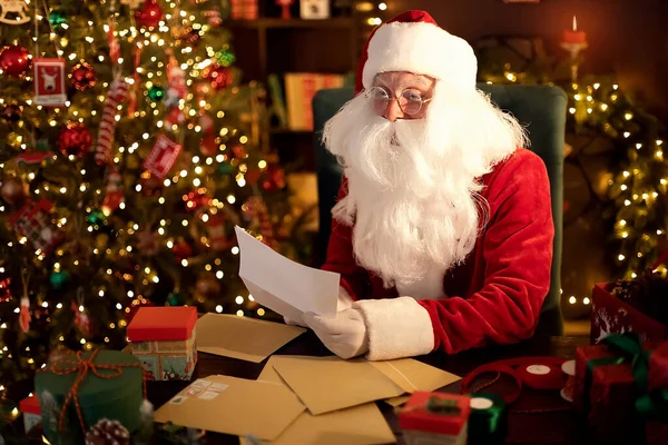Der Weihnachtsmann bereitet zu Hause am Schreibtisch Geschenke für Kinder für Weihnachten vor, während er Wunschzettel liest — Stockfoto