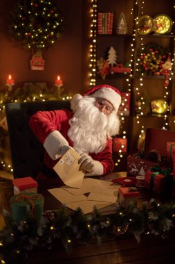 Noel Baba, Noel Baba 'nın evindeki masasında çocuklar için hediyeler hazırlarken bir yandan da mektubu çıkarıyor.