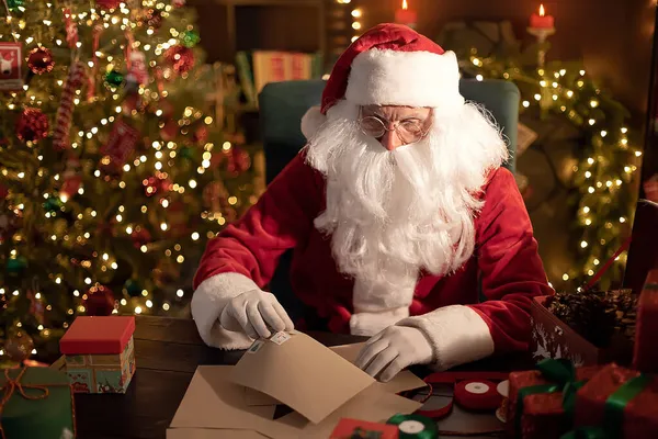 Weihnachtsmann bereitet zu Hause am Schreibtisch Geschenke für Kinder für Weihnachten vor und blättert in Briefen — Stockfoto