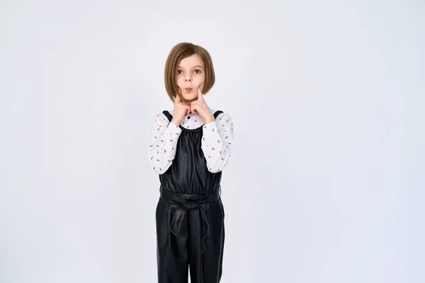 Маленька дівчинка в чорно-білому одязі стоїть на білому тлі, жестикулюючи обличчям — стокове фото