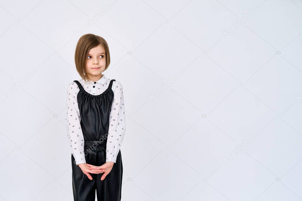 Little child girl in black white clothes stands over white background while looking sideways 