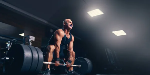 Emocjonalny starszy powerlifter przygotowujący się do ćwiczeń deadlift ze sztangą na treningu crossowym w siłowni — Zdjęcie stockowe