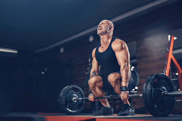 Бодібілдер м'язистий чоловік робить важкі вправи підйом з вагою, перебуваючи в спортзалі в темряві — стокове фото