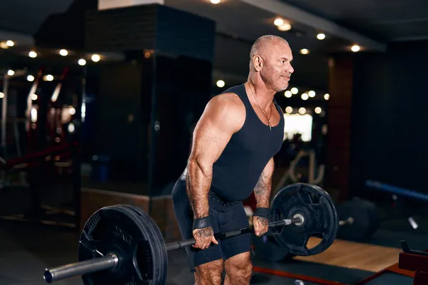 Дорослий лисий культурист м'язистий чоловік робить важкі вправи підйом з вагою, перебуваючи в спортзалі в темряві — стокове фото