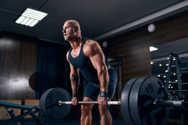 Yaşlı bir kaldırıcı spor salonunda çapraz antrenman yaparken halterle kaldırma egzersizi yapıyor. Vücut geliştirme 