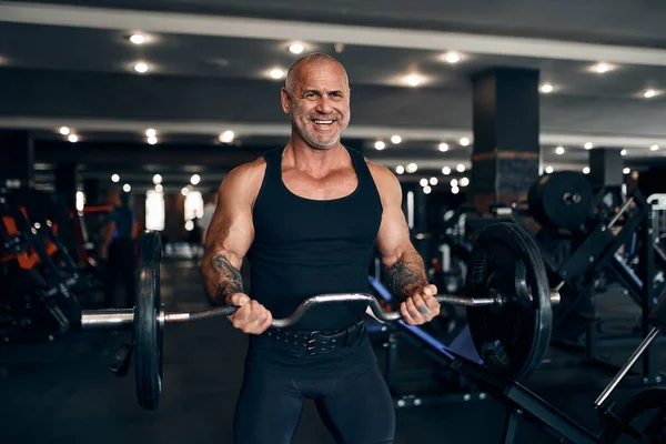 М'язистий лисий чоловік, який працює в тренажерному залі, виконує вправи з барбелом на біцепсах. Концепція бодібілдингу — стокове фото