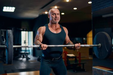 Spor salonunda halterle antreman yaparken kaslarını şişiren yetişkin bir vücut geliştirici. Vücut geliştirme kavramı