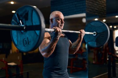 Yaşlı vücut geliştirici sporcu kaslarını şişirirken spor salonunda antrenman yapıyor. Halterli bir sporcu.