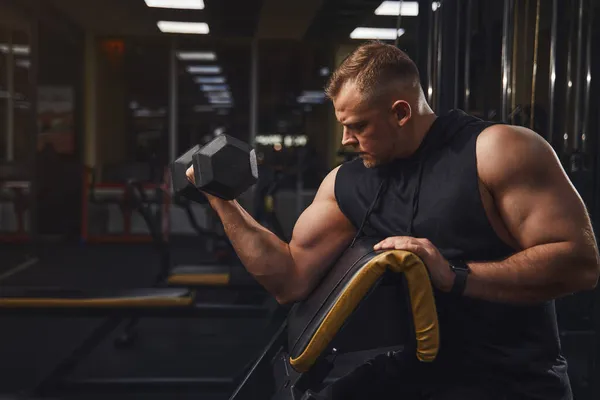 Hombre deportivo con grandes músculos y amplios trenes traseros en el gimnasio con pesas mientras balancea bíceps —  Fotos de Stock