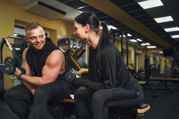 Bodybuilder man Personal trainer tonen jonge vrouw hoe om te trainen biceps in de sportschool met halters — Stockfoto