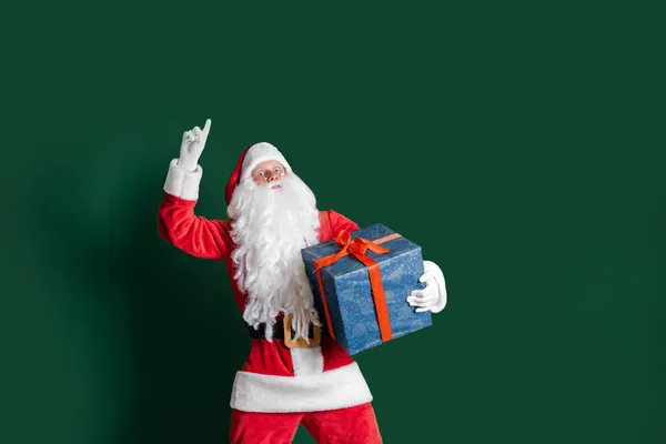 Emotionaler Schauspieler im Kostüm des Weihnachtsmannes hält Zeigefinger auf grünem Hintergrund in die Höhe — Stockfoto