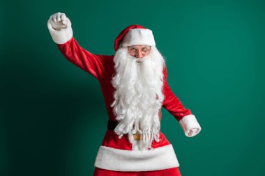 Yeşil arka planda dans ederken uzun sakallı, Noel Baba kostümü giymiş komik bir aktör.