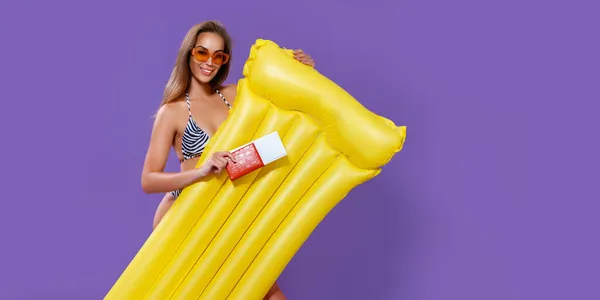 Smiling girl ready to summer vacations shows tickets with passport while holding inflatable mattress — Stock Photo, Image