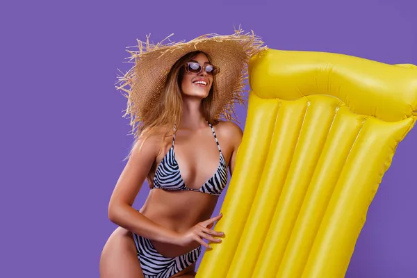 Beautiful happy blonde girl in bikini with animal print holds summer mattress on purple background — Stock Photo, Image