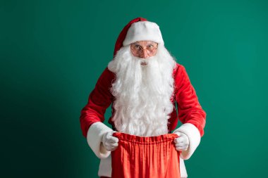 Noel zamanı. Noel Baba yeşil arka planda hediyelerle dolu bir çanta tutuyor ve açıyor. Yeni yıl konsepti.