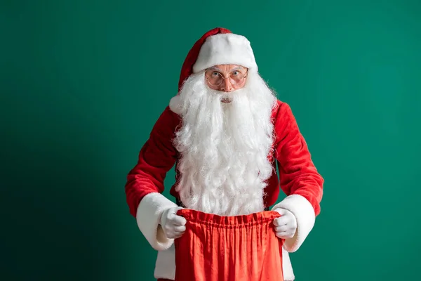 Weihnachtszeit. Der Weihnachtsmann hält und öffnet eine Tüte mit Geschenken auf grünem Hintergrund. Neujahrskonzept. — Stockfoto