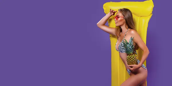 Sarı şişme şilteli bikinili güzel bir kadın ananas tutarken dışarı bakıyor.. — Stok fotoğraf