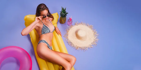 Draufsicht hübsches erwachsenes Mädchen trägt Bikini liegt auf aufblasbarer Matratze isoliert auf lila Hintergrund — Stockfoto