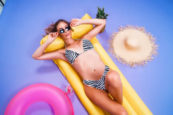 Von oben attraktive Frau trägt Bikini liegt auf aufblasbarer Matratze isoliert auf lila Hintergrund — Stockfoto