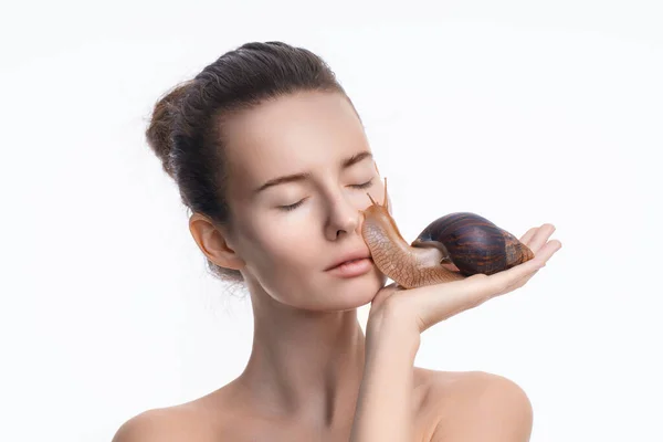 Gyönyörű fiatal nő csigával az arcán, fehér háttér mellett. Öregedés elleni kozmetikai kezelések — Stock Fotó