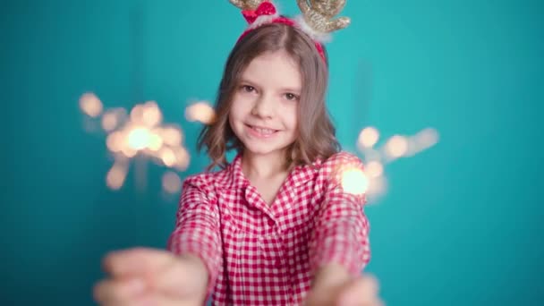 Щаслива маленька дівчинка з захопленням дивиться на палаючого іскриста в руці на синьому фоні — стокове відео