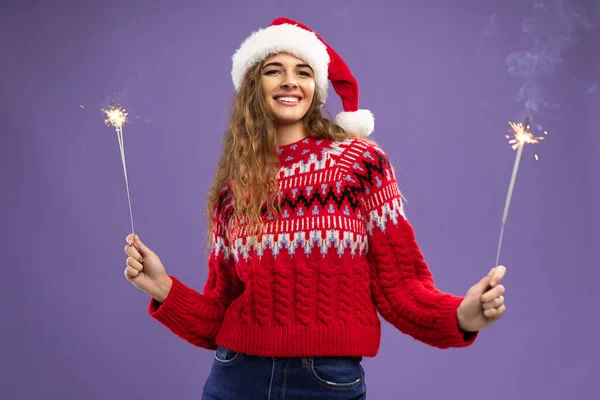 Smiling beaty Santa curly young woman holds burning sparklers in studio shot on purple background — Stock Photo, Image