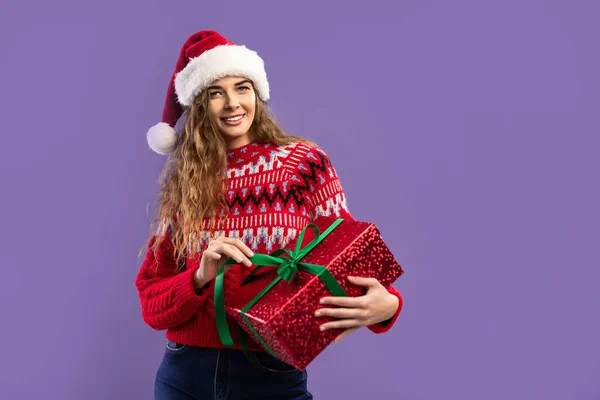 Happy smiling caucasian girl wears Santa hat holds gift box on purple background. Christmas party — Stock Photo, Image