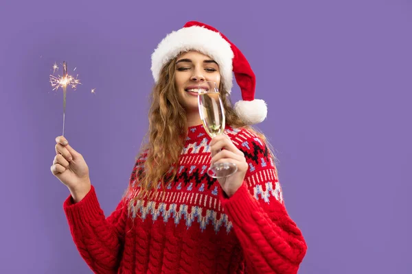 Happy girl wears Santas hat drinks champagne holds sparkler on purple background. Christmas party — Stock Photo, Image