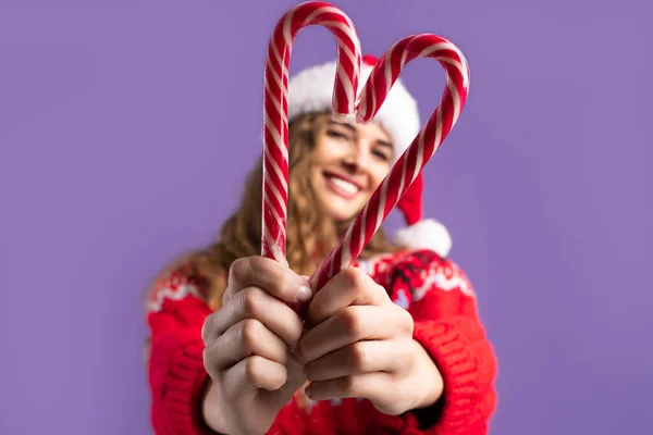 Selective focus. Happy girl wears in Santa hat makes heart from candys. Christmas concept. — Stock Photo, Image