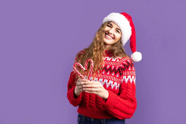 Happy girl wears in Santa hat makes heart from candys. purple background. Christmas concept — Stock Photo, Image