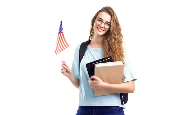 Smiling student girl in glasses with backpack holds books, notebooks and flag USA on white background — Stock Photo, Image