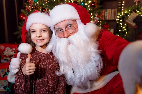 Père Noël fait selfie avec charmante petite fille qui montre pouce vers le haut. Fond de Noël — Photo
