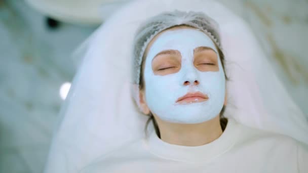 A menina com uma máscara azul aplicada em seu rosto e relaxar. Cuidados com a pele na clínica de beleza ou salão de beleza — Vídeo de Stock