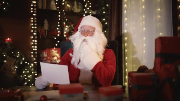Emocjonalny Święty Mikołaj czyta list i rozmawia z kamerą siedząc przy stole — Wideo stockowe