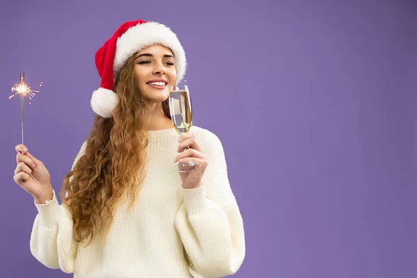 Attractive girl wears in santa hat with glass of champagne and sparkler on violet background — Stock Photo, Image