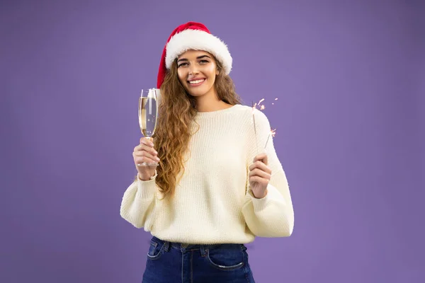 Portrait of happy girl wears in santa hat with glass of champagne and sparkler on violet background — Stock Photo, Image