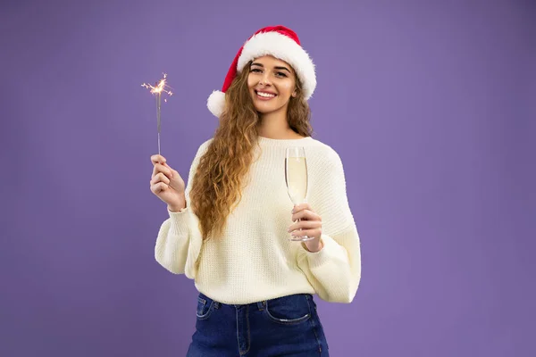 Happy Santa girl wears in white sweater holds glass of champagne and sparkler on violet background — Stock Photo, Image