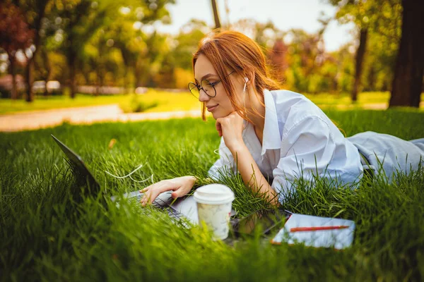 Студент молодої дівчини в окулярах готується до іспитів, використовуючи ноутбук на траві. Концепція освіти — стокове фото