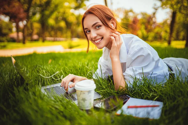 Красива усміхнена дівчина в парку на відкритому повітрі використовує ноутбук, лежачи на траві. Концепція освіти . — стокове фото
